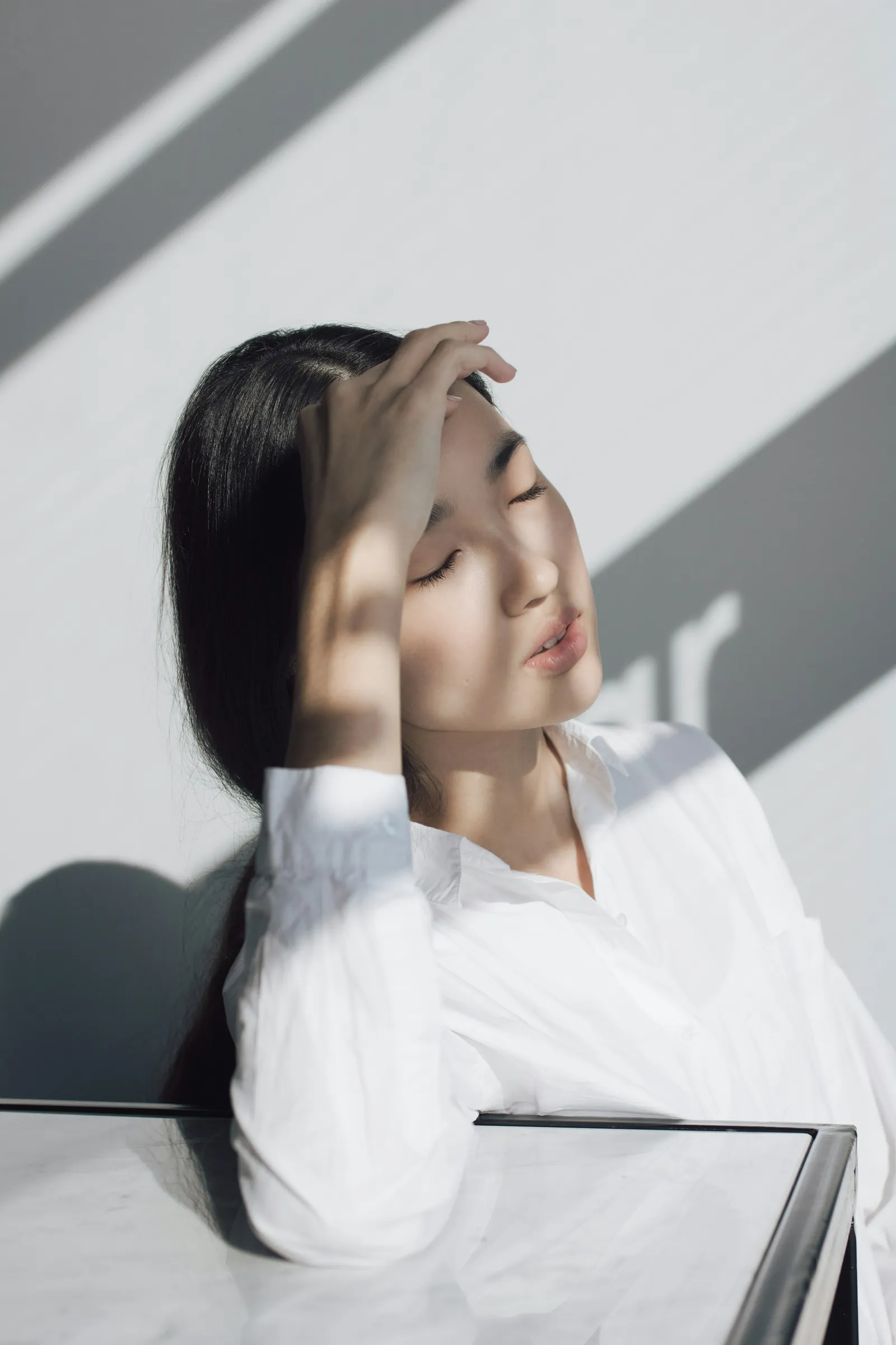 흰 벽에 비친 창 그림자 앞에서 이마에 손을 얹은 사람
